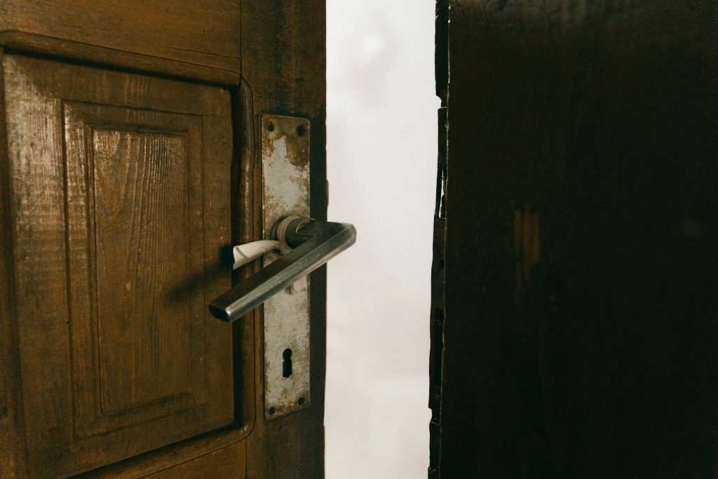 A rustic wooden door slightly ajar with a metal handle, creating a mysterious ambiance.
